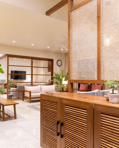 Wooden cabinet with cane screen divider opening to a warm living room in a Pune home