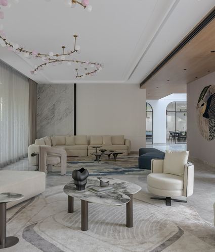 Neutral-toned living room with curved sofa, marble tables, and branch-form pendant light, arched doorway beyond