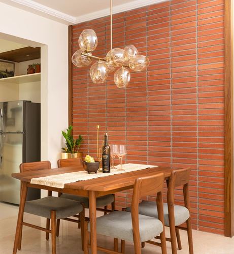 Dining table with wooden chairs beneath a bubble chandelier against a brick feature wall