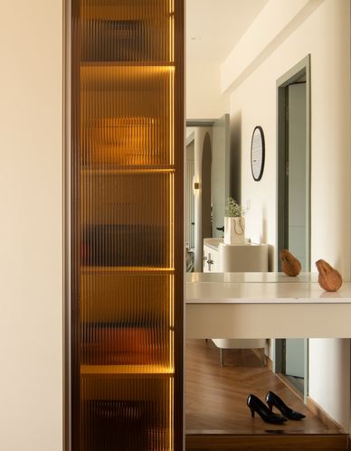 Backlit fluted amber glass cabinet beside a console table reflecting an archway in a home entry.
