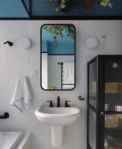White subway-tiled bathroom with black pedestal sink fixtures and mirror reflecting blue ceiling