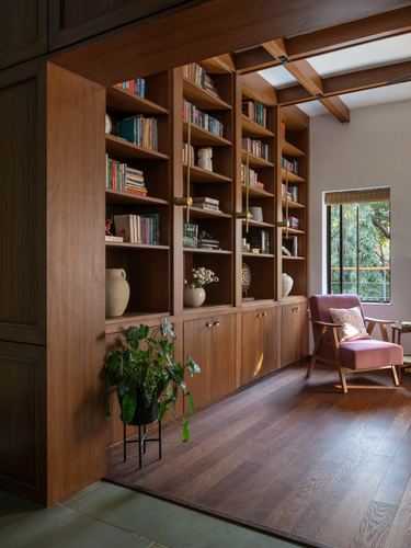 Wooden library nook with built-in shelving, ceramics, plant stand and pink armchair by window