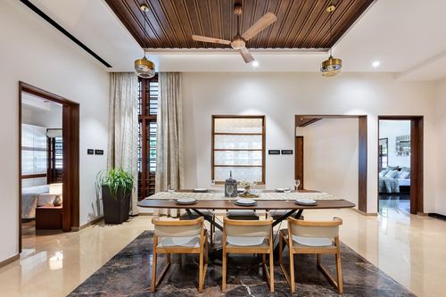 Dining room with wooden ceiling, brass pendants, dark table, and marble floor rug