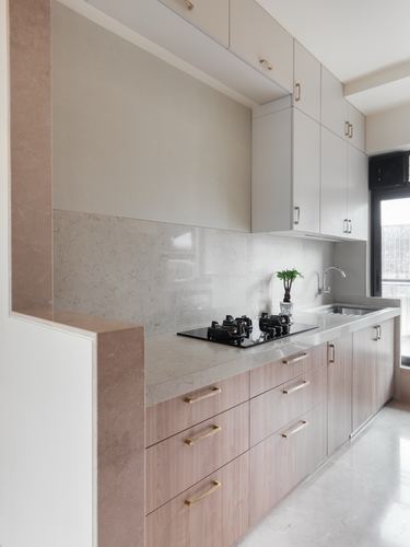 Minimal kitchen with pink stone backsplash, wood cabinetry and brass handles, black hob in view