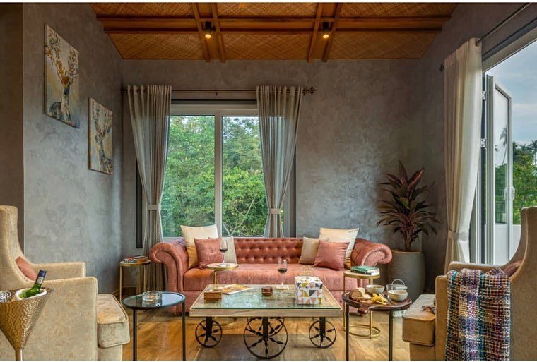 Living room with pink tufted sofa, glass-and-metal coffee table, and large window overlooking greenery in Goa home