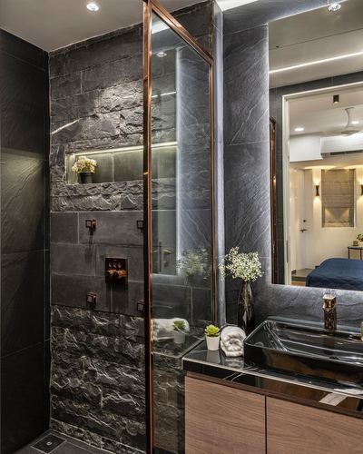 Dark stone-clad shower with brass fixtures and mirror reflecting an adjoining bedroom