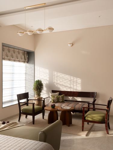 Sunlit living room with dark wood chairs, olive cushions, and a brass bubble pendant light