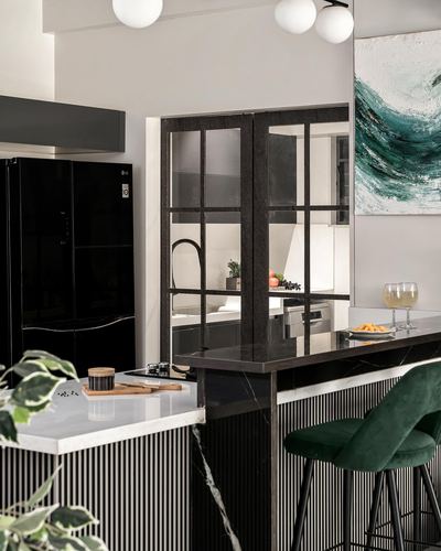 Monochrome kitchen with fluted island, marble countertop, green velvet stools, and internal glass door