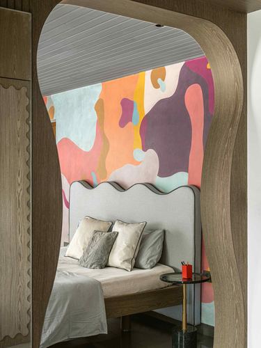Curved wooden archway framing a bed with wavy grey headboard against a colorful abstract mural