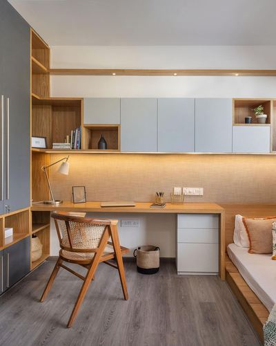 Wooden study desk with cane chair beneath open shelving and grey cabinets in a bedroom nook