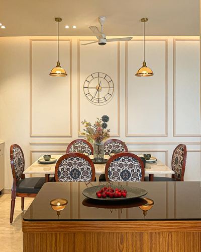 Dining room with marble table, patterned chairs, brass pendant lights, and wall clock, foreground kitchen island with cherries