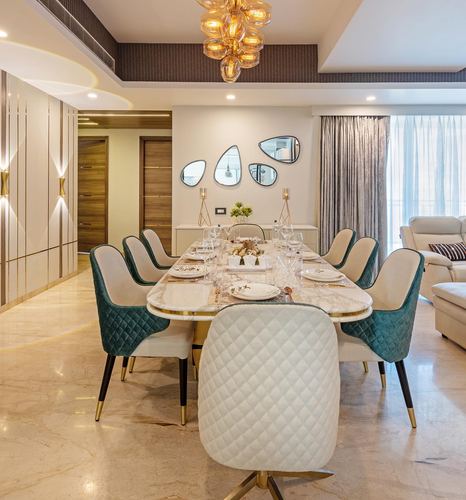 Dining room with oval marble table, teal and cream quilted chairs, amber chandelier and mirror cluster