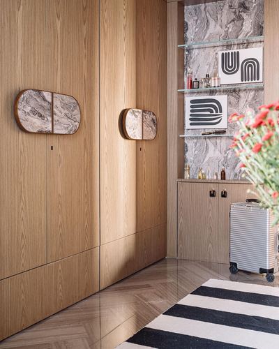 Wood-panelled foyer with two capsule mirrors, marble-clad shelving niche, and a striped rug