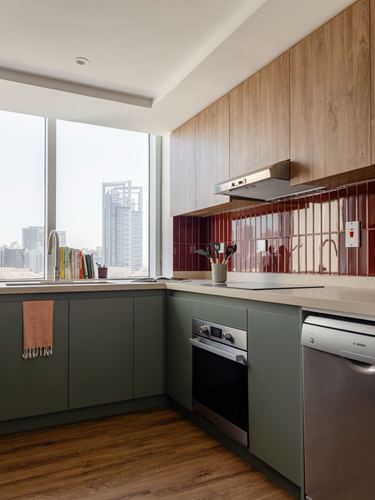 L-shaped kitchen with green base cabinets, wood upper cabinets, red tile backsplash, city view window