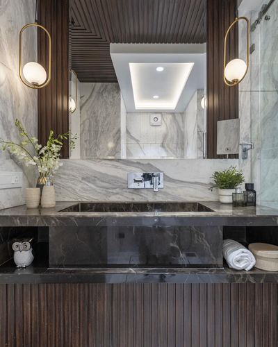 Marble vanity with dark stone counter, fluted wood panels, and brass pendant lights in luxe bathroom