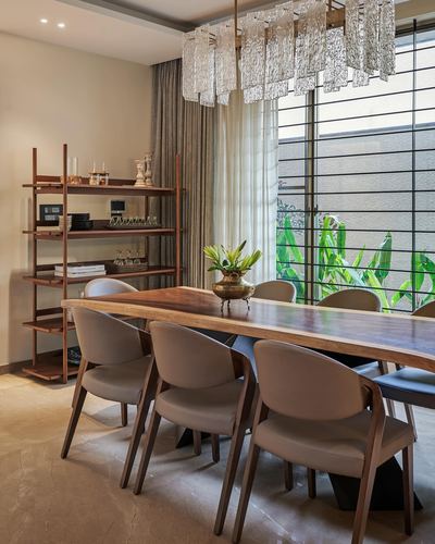 Dining room with live-edge wood table, taupe chairs, crystal chandelier and view to greenery