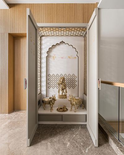 Open cabinet reveals arched pooja niche with brass deities and jali screen