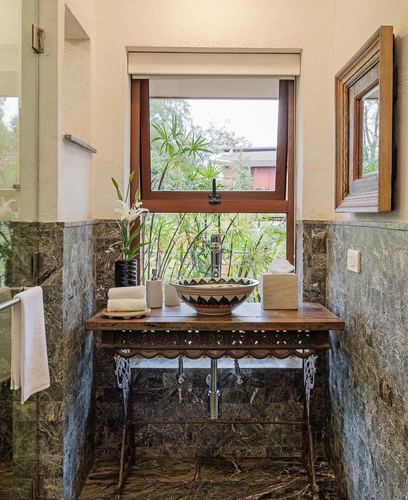 Bathroom vanity with patterned vessel sink on carved console below a window overlooking greenery