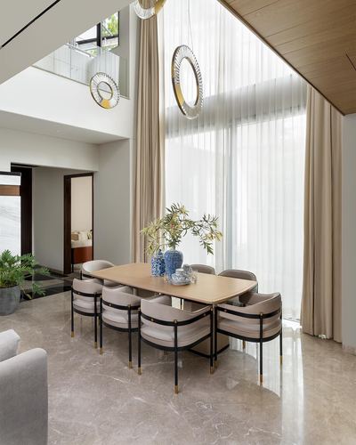 Double-height dining room with round table, cushioned chairs, sheer curtains and round mirrors above