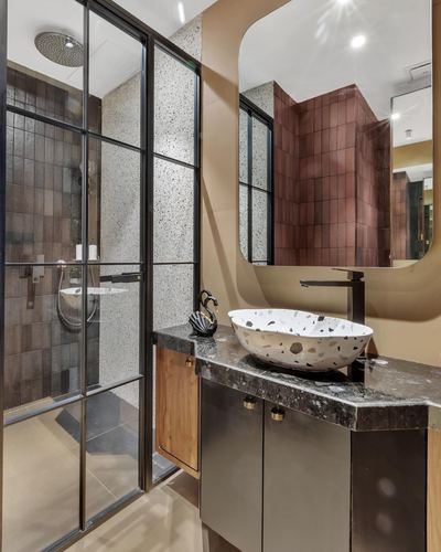 Bathroom with terrazzo vessel sink, black-framed glass shower, arched mirror and tiled walls