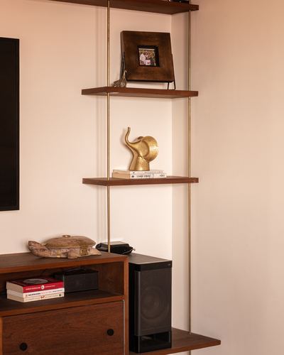 Wall-mounted wood shelves on brass rods with a brass elephant figurine above a wooden sideboard