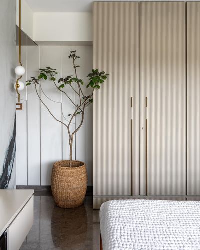 Beige fluted wardrobe beside potted plant in woven basket on marble floor