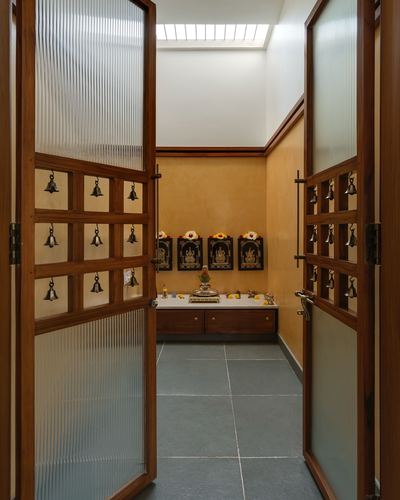 View through open wooden doors with reeded glass and bells into a mustard-walled pooja room