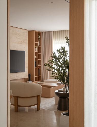 View through a wooden doorway into a minimalist living room with stone-clad TV wall and cane-toned furniture