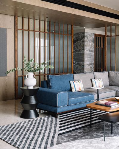 Living room with blue and grey sectional sofa, striped rug, and wood-framed glass partition wall