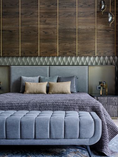 Bedroom with wood-panelled brass-lined wall, grey headboard, mustard pillows, tufted bench