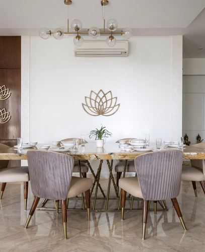Dining table with mauve velvet chairs beneath a lotus wall sculpture and bubble chandelier