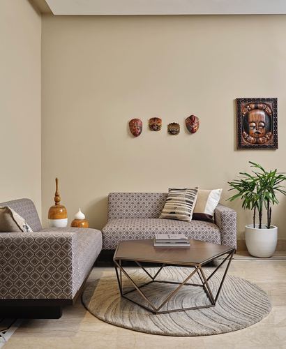 Beige living room with patterned sofas, tribal masks on wall, geometric coffee table on round rug