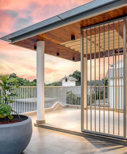 Terrace with wood-clad ceiling, round column, and metal slat screen against a pink sunset sky
