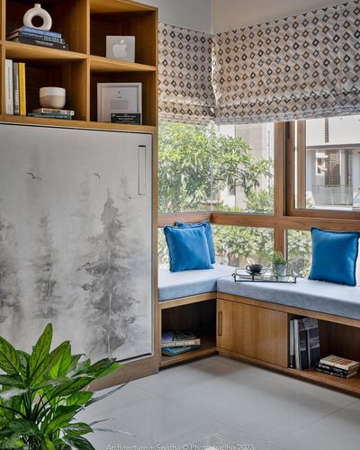 Wood-paneled corner window seat with blue cushions beside built-in bookshelf and greenery view