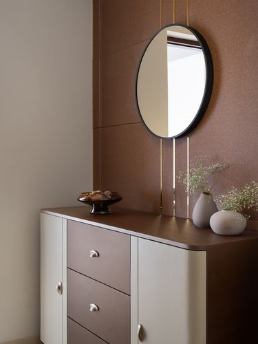 Round black-framed mirror on textured brown wall above cream and brown console with vases