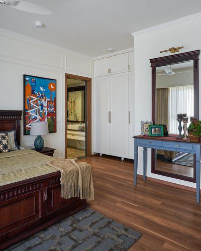 Bedroom with dark wood bed, colorful wall art, white wardrobe, and carved mirror over blue dressing table