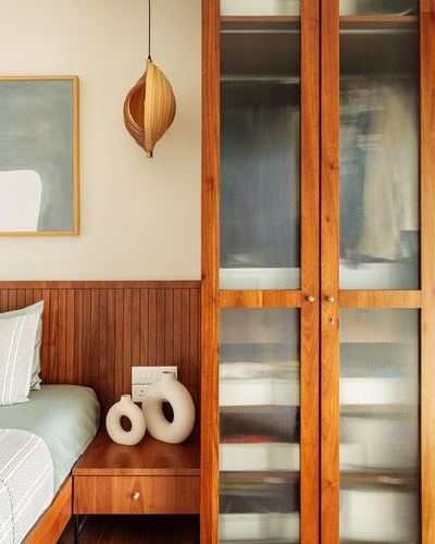 Bedroom corner with wood-panelled headboard, ribbed glass wardrobe doors, pendant light and ceramic vases