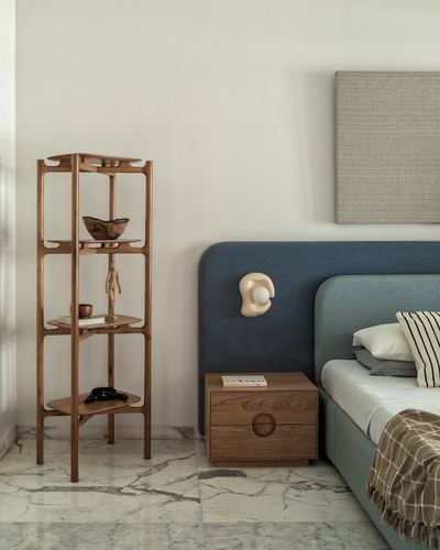 Bedroom corner with wooden shelving unit, blue upholstered headboard, and wooden nightstand on marble floor