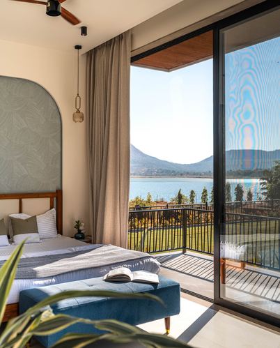 Bedroom with arched sage headboard, blue bench, and glass doors opening to lake and mountain view