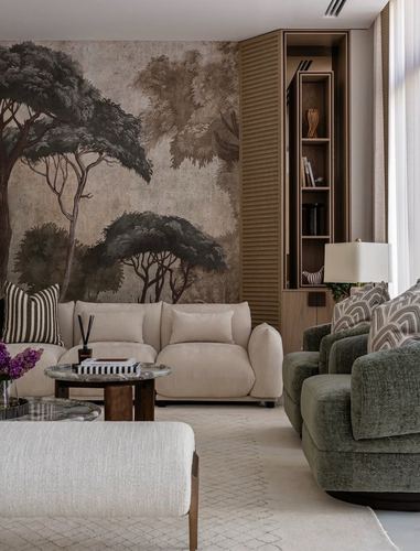 Living room with tree mural wall, cream sofa, green armchairs, and wooden shelving unit