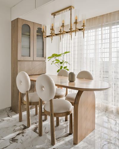 Sunlit dining nook with oval wood table, cream donut-back chairs, and brass chandelier