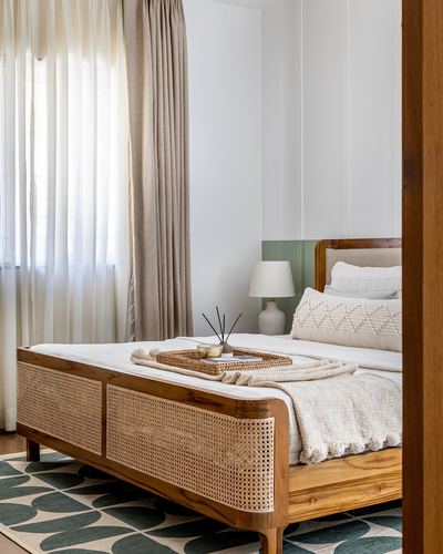 Wooden bed with woven cane panels, white bedding, sheer curtains and green wall trim in bedroom