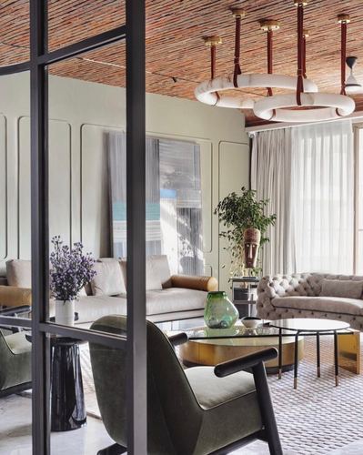 Living room seen through black steel-framed glass door with tufted sofas, sculptural chandelier and woven ceiling
