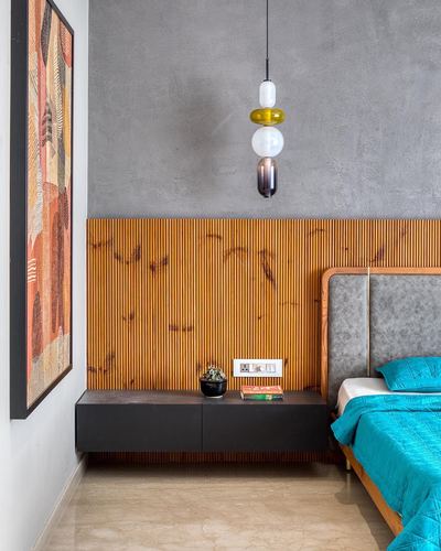 Bedroom corner with fluted wood panel, black floating console, layered glass pendant and teal bedspread