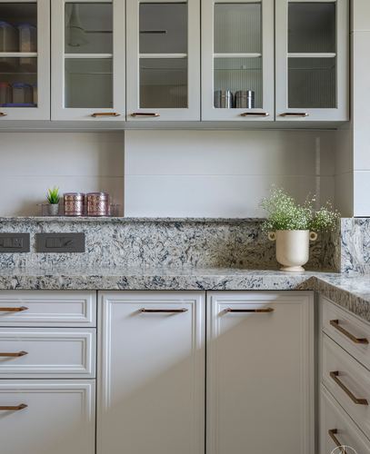 Kitchen counter with granite backsplash, glass cabinets, and copper canisters near a flower vase