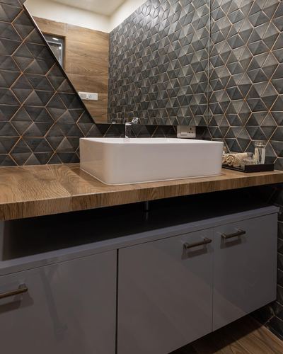 Bathroom vanity with square white sink on wood counter against geometric tiled wall