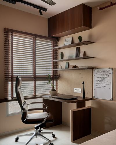 Home study corner with wooden desk, floating shelves, whiteboard, and black leather office chair by a window