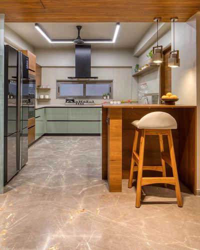 L-shaped kitchen with sage green cabinets, wood-clad breakfast counter, black chimney hood and stone flooring