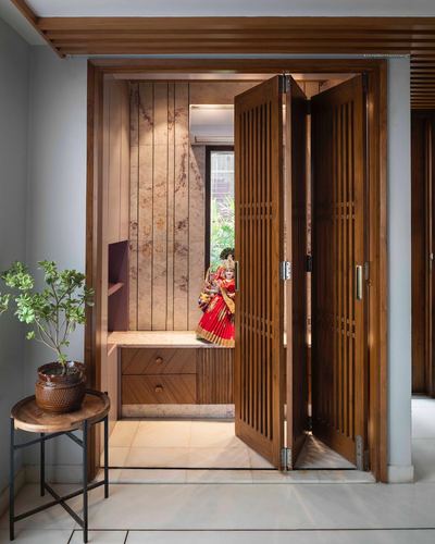 Pooja alcove with slatted teak doors, stone walls, and a dressed deity figure niche