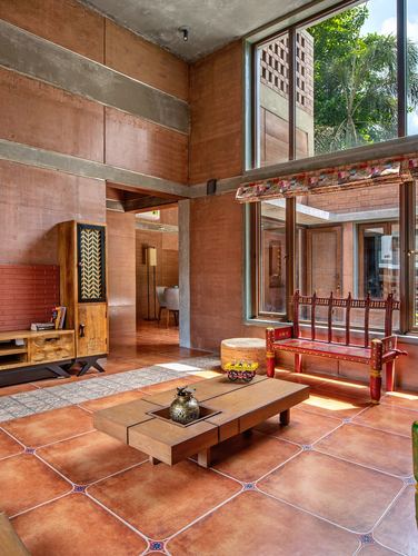 Double-height living room with rammed earth walls, terracotta floor, and carved wooden bench by window